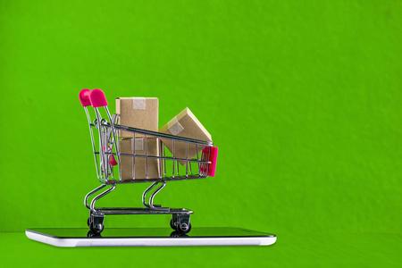 网上购物, 电子商务或订单在线概念: 购物车与产品纸箱上的绿色平板